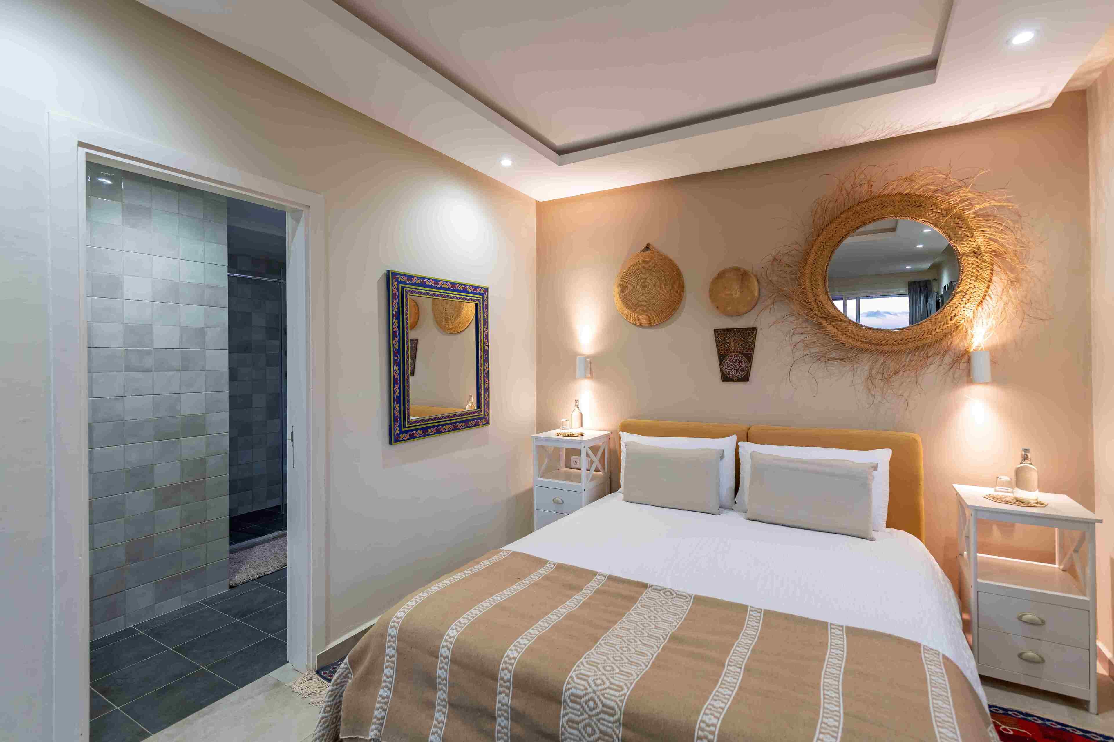A bedroom with a bed, bedside tables, a mirror, and decorative wall hangings.