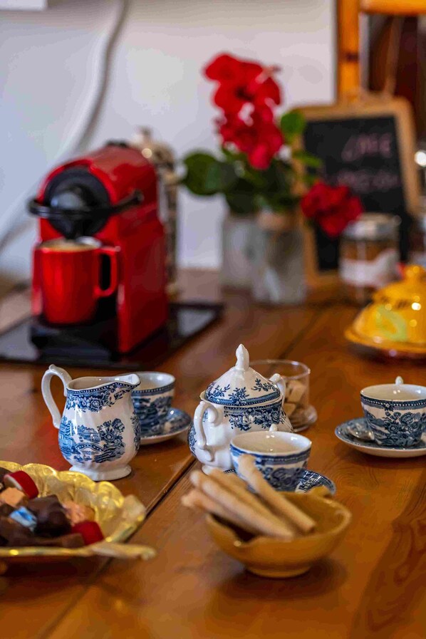 Ein Tisch ist mit blauen und weißen Porzellantassen, einem Teekessel und einer roten Kaffeemaschine gedeckt.