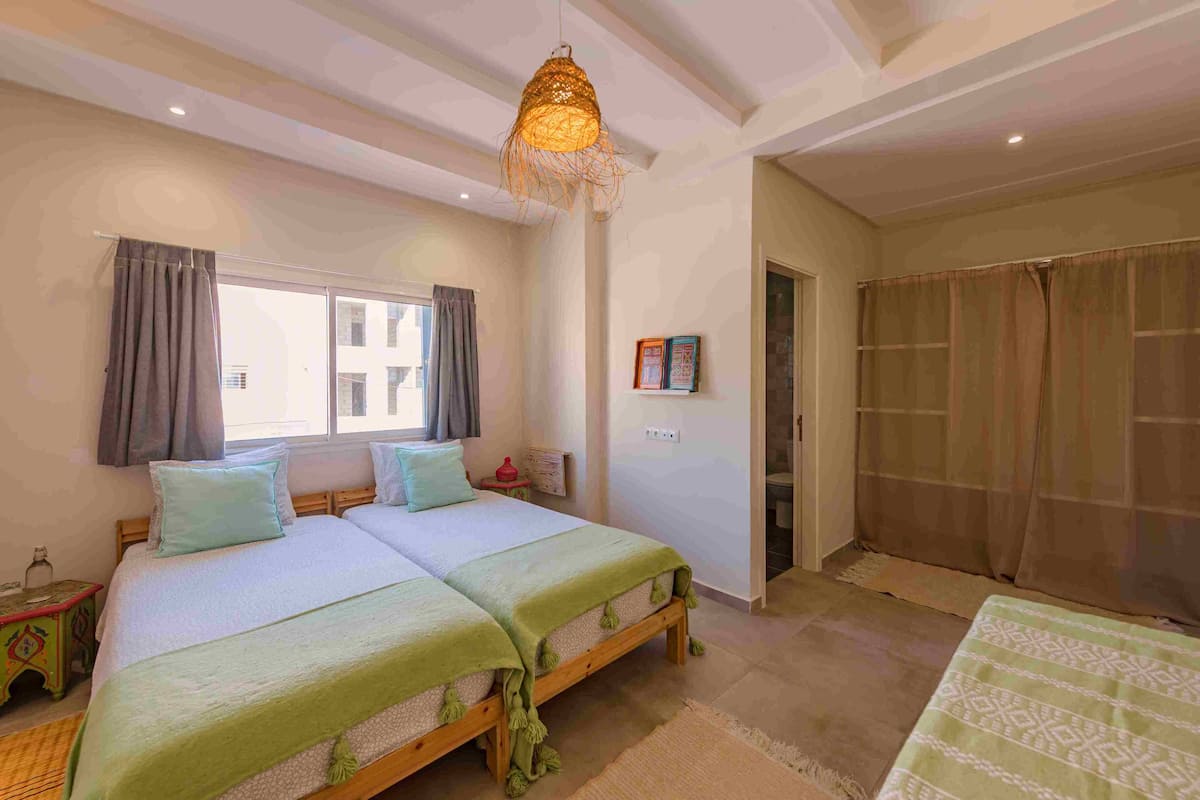 Un lit double avec une couvre-lit verte et un luminaire suspendu au-dessus.