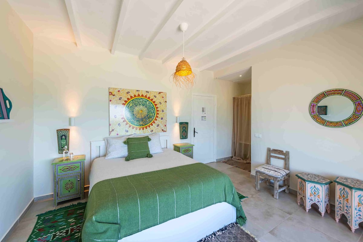 Une chambre à coucher avec un lit, un luminaire suspendu, une chaise et une petite table.