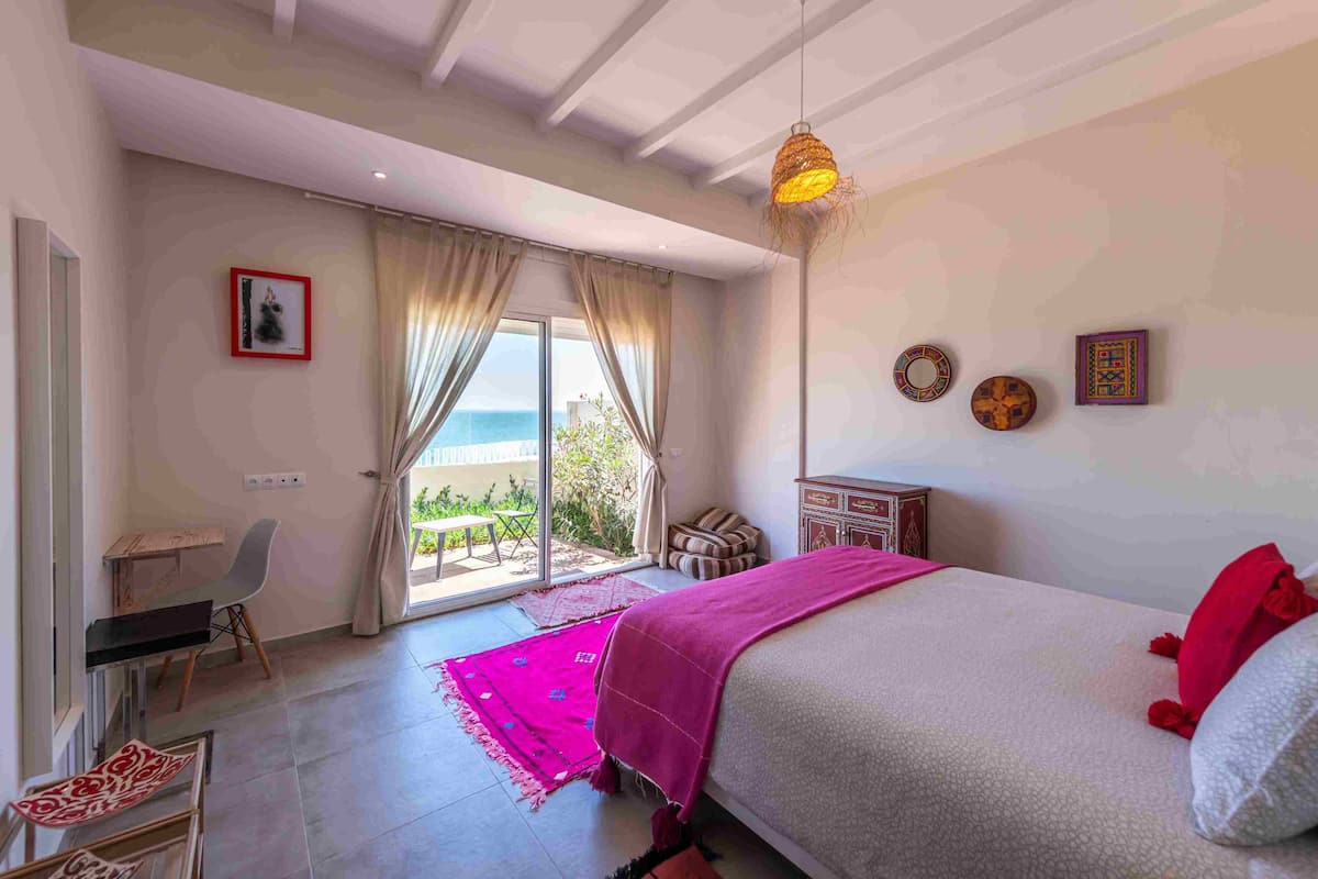 Une chambre à coucher comprenant un lit, un bureau, une chaise, une fenêtre avec des rideaux et une vue sur l’extérieur.