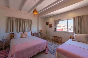 Un dormitorio con dos camas, una ventana con cortinas, una mesita y una lámpara decorativa colgante.