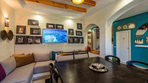 Una sala de estar moderna con una mesa de comedor de madera oscura, un sofá y un televisor grande montado en la pared.