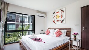 Ein modernes Hotelzimmer mit einem großen Bett, einem kleinen Tisch, einer Wand-Klimaanlage und einem großen Fenster mit Blick auf ein Gebäude und Palmen.