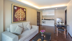 Ein Wohnzimmer mit einer Couch, einem Couchtisch und einem Bild an der Wand. Im Hintergrund ist eine Küche mit Schränken und einem Kühlschrank zu sehen.