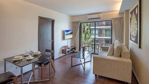 Ein modernes Wohnzimmer mit Essbereich, einer Couch, einem Fernseher und einem Balkon mit Blick auf Gebäude.