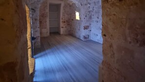 Un estrecho pasaje con suelo de madera y paredes de piedra, que lleva a una puerta al final.