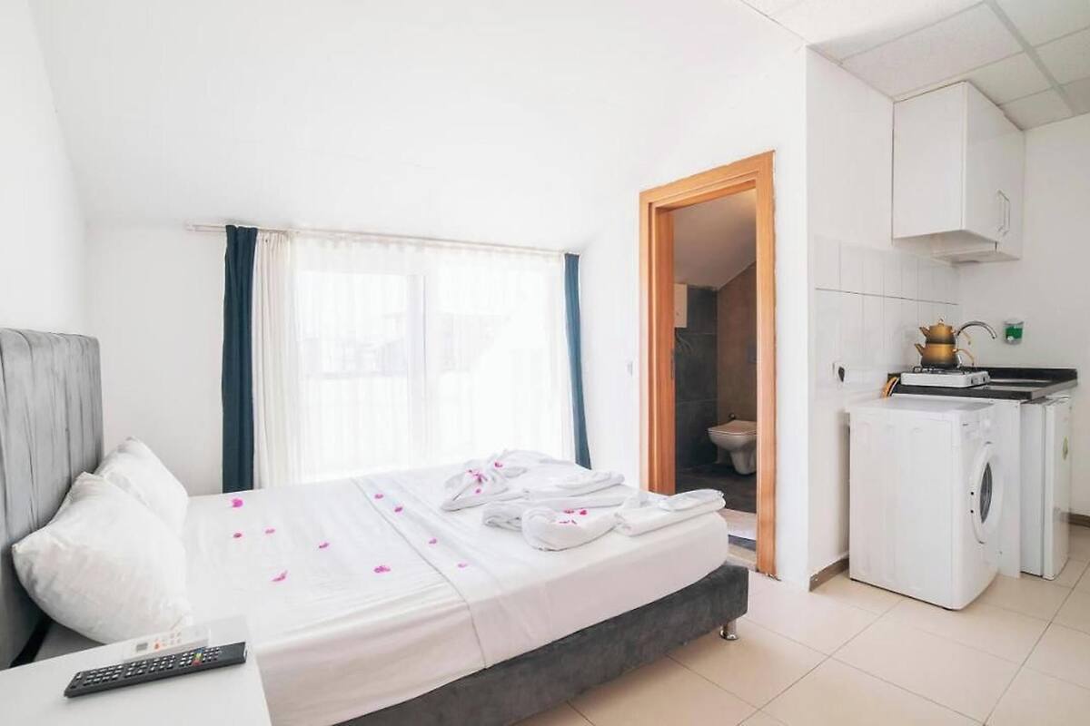 A hotel room with a bed, a remote control, a kitchenette, and a bathroom visible through an open door.