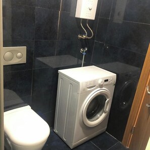 Un baño peque ño con lavadora, inodoro y toma de corriente en la pared.