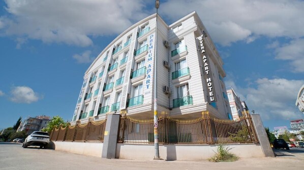 Un hotel de varios pisos con un llamativo letrero que dice "Premium Apart", con balcones y una entrada con portón.