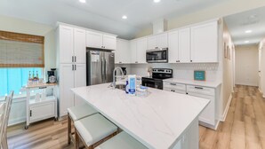 A modern kitchen with white cabinets, a large island, stainless steel appliances, and a coffee bar.