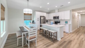 A modern kitchen with white cabinets, a central island with stools, and a dining area with a table and chairs.