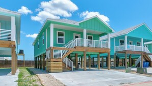 A beachfront property with multiple green buildings, wooden decks, and a clear sky.