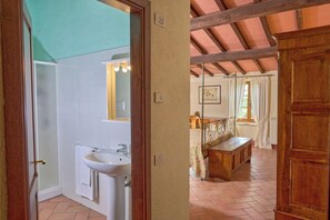 A bathroom with a sink and mirror, a wooden bench in a bedroom, and a door leading to another room. - Agriturismo Le Case (Castiglione d'Orcia)