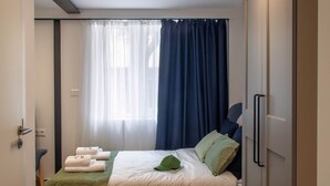 Ein gemütliches Schlafzimmer mit Bett, Nachttisch, Kleiderschrank, einem Fenster mit Vorhängen und einer Deckenleuchte.
