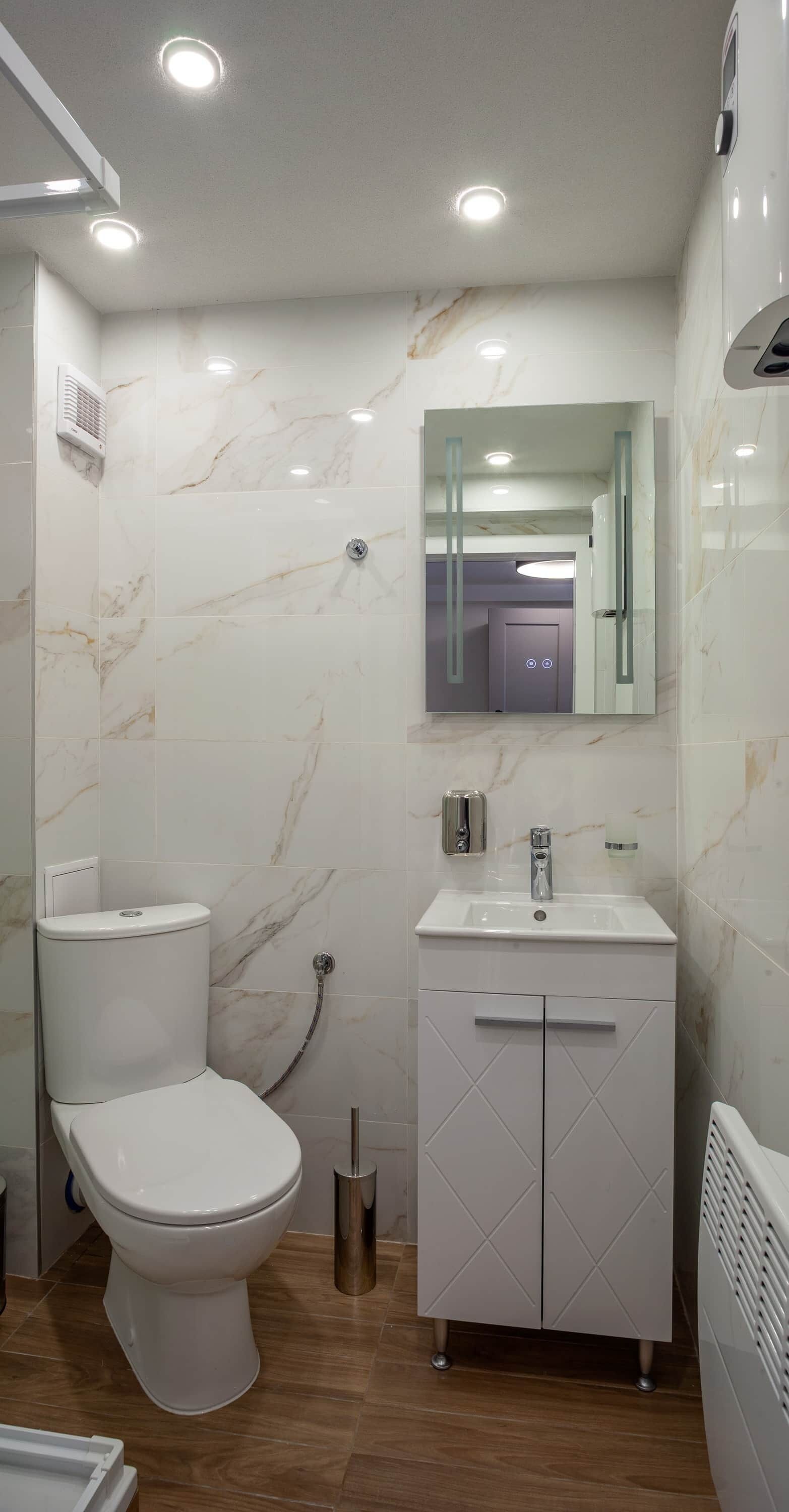 A bathroom with a toilet, sink, mirror, and marble tiles.