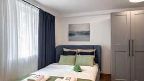 Ein Hotelzimmer mit einem Bett, einer grünen Decke, zwei Handtüchern mit einem Logo, einer grünen Kappe, einem Bild an der Wand und einem Schrank.