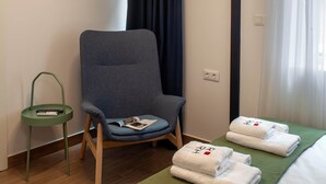 Ein Hotelzimmer mit einem Bett, einem Sessel, einem kleinen Tisch, einer Uhr und einem Fenster mit Vorhängen.