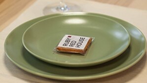 Une table avec une assiette verte, un verre d’eau et un petit paquet étiqueté « RUBI RED HOUSE ».