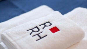 Une serviette blanche pliée, ornée de lettres brodées « RH » et d’un carré rouge sur un fond bleu.