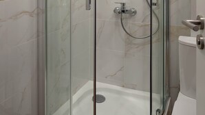 Une cabine de douche fermée par des parois en verre, avec des toilettes sur le côté droit.