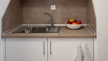 A kitchen with a stainless steel sink, a bowl of fruit, and a towel hanging on the wall.