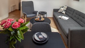 Ein modernes Wohnzimmer mit einer Couch, Sesseln, einem Couchtisch und einem Esstisch mit einem Blumenstrauß.