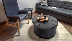 Ein modernes Wohnzimmer mit hohen Decken, freiliegenden Holzbalken, einer Couch, einem Sessel, einem kleinen Tisch mit Tablett und einem runden Glastisch.