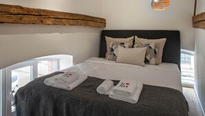 Ein modernes Hotelzimmer mit einem großen Bett, zwei runden Fenstern, einer Holzbalkendecke und einer Pendelleuchte.