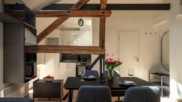 Eine moderne Küche mit weißen Schränken, ein Essbereich mit Tisch und Stühlen sowie freiliegende Holzbalken.