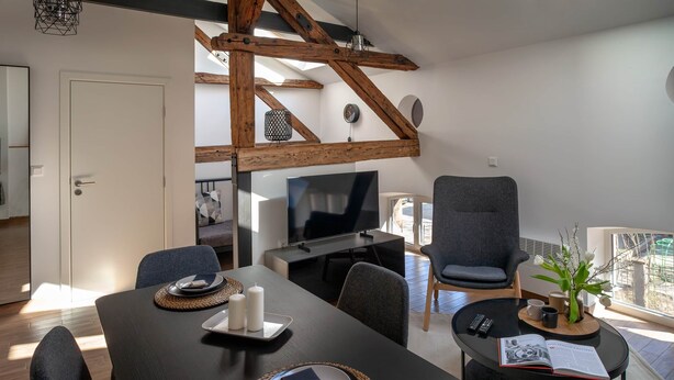 A modern living room with a dining area, wooden beams, a TV, and a large window.