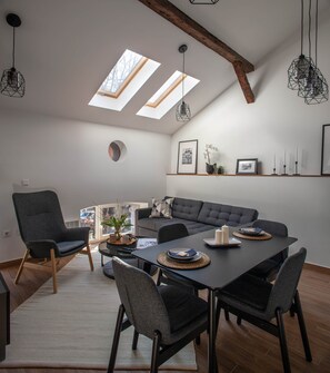A modern living room with a dining table, grey sofas, and a large window with skylights.