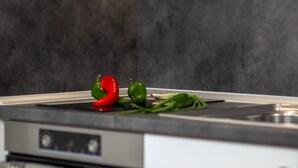 A kitchen with a modern design, featuring a stainless steel oven, a white cabinet, and a countertop with a red pepper and green vegetables.