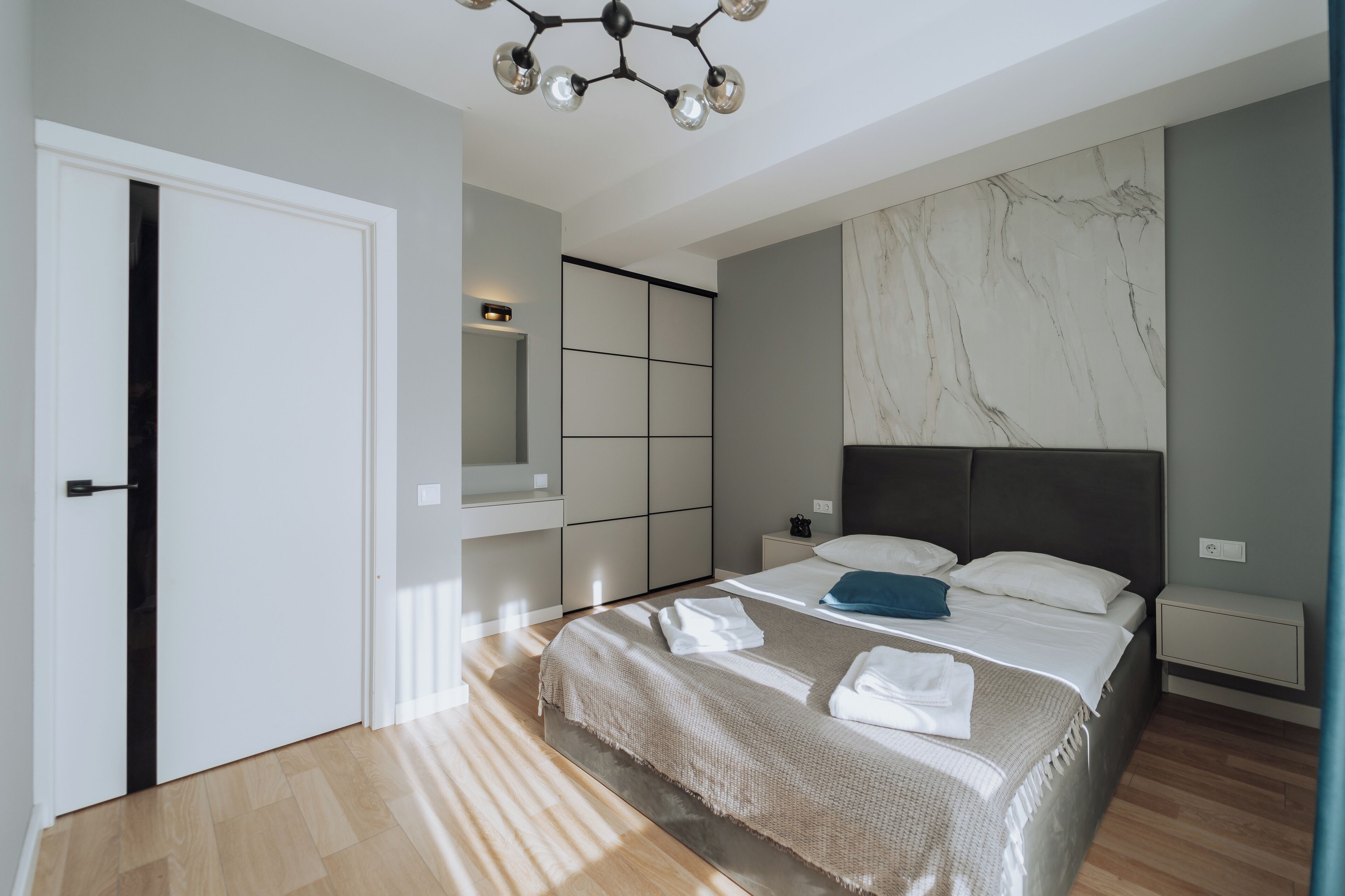 A modern bedroom with a large bed, built-in wardrobe, and a marble accent wall.