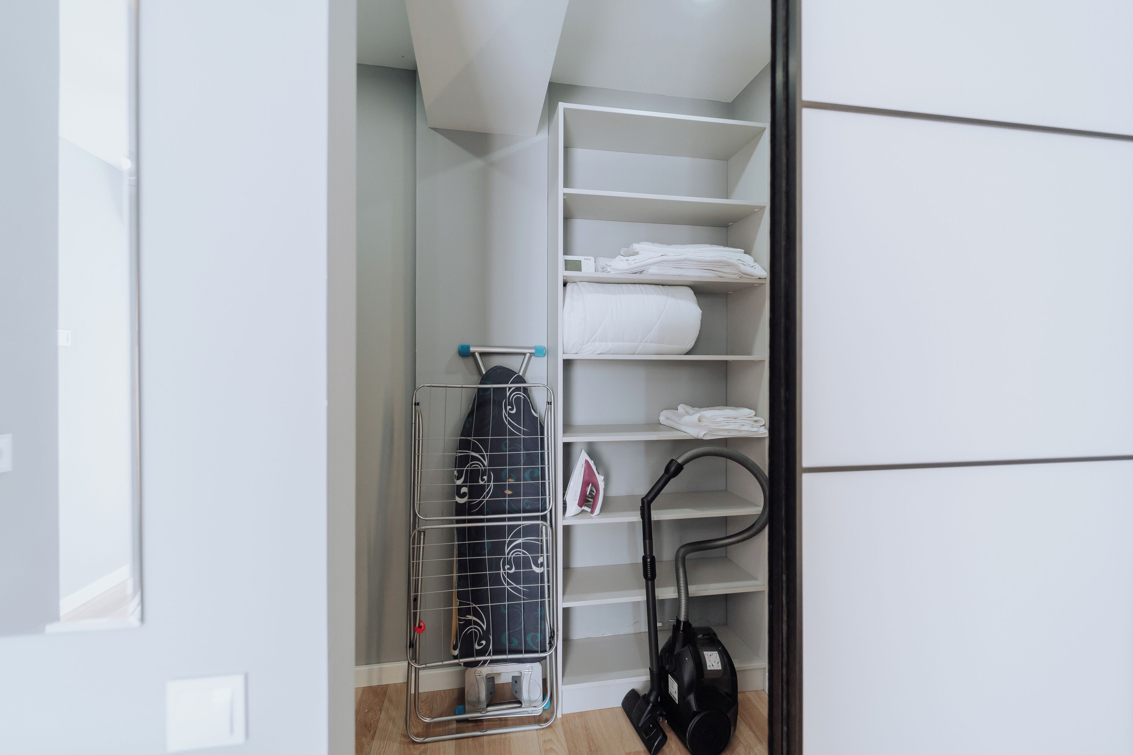 Een netjes opgeruimde kast met planken voor opgevouwen kleding, een kledingroede en een stofzuiger.