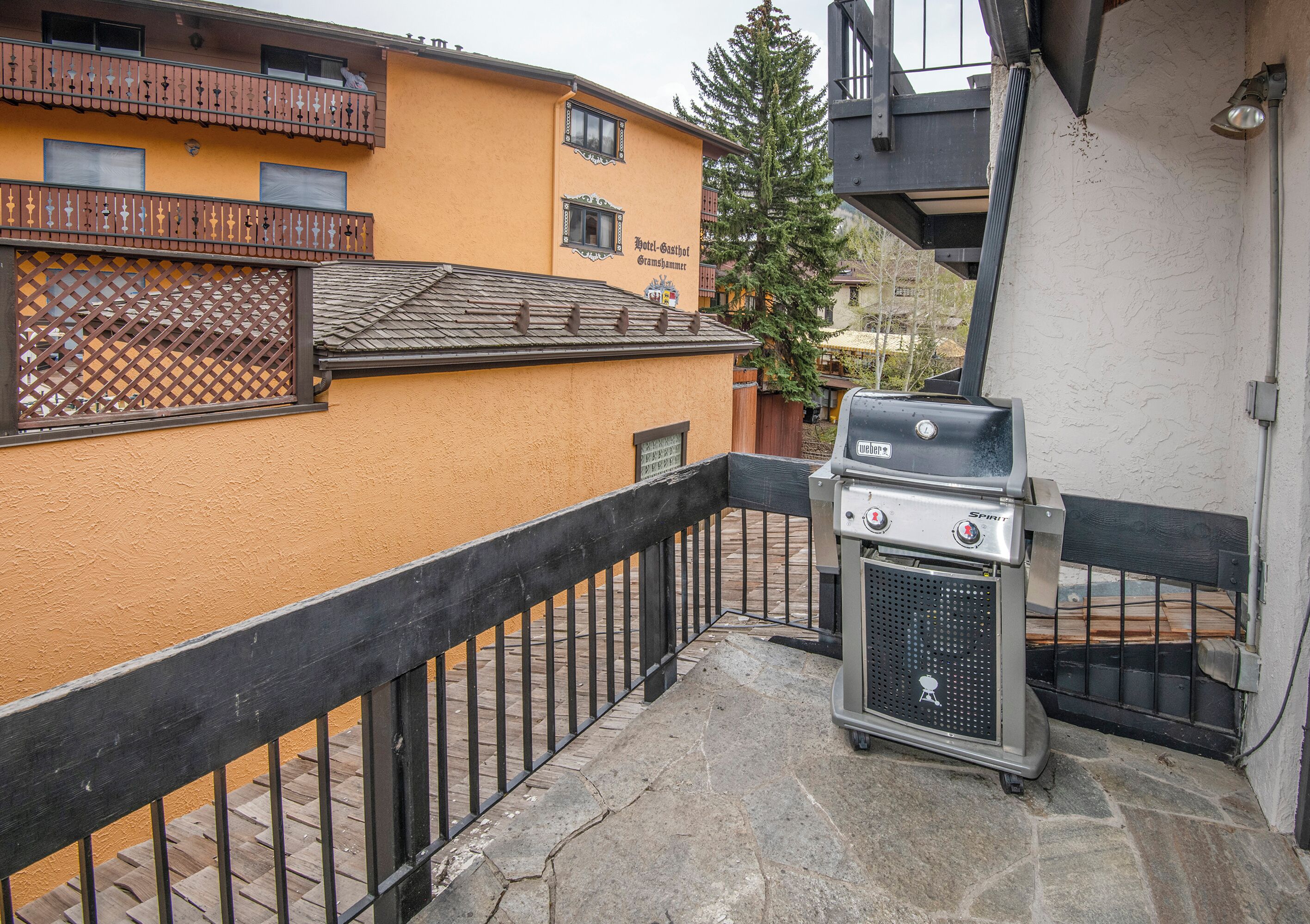 Un balcon avec un barbecue Weber, un sol en pierre et, en arrière-plan, un immeuble jaune doté de balcons.