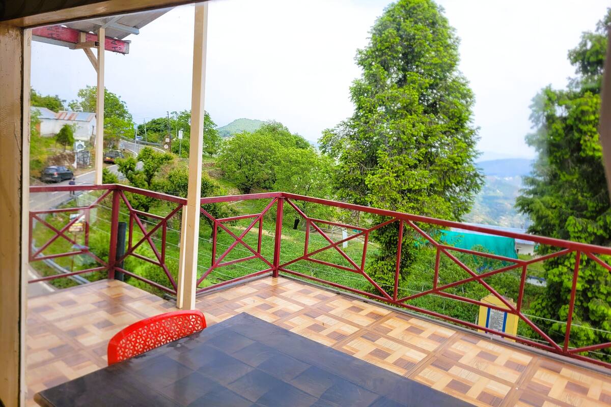 A balcony with a red railing, a wooden floor, and a table with a chair.