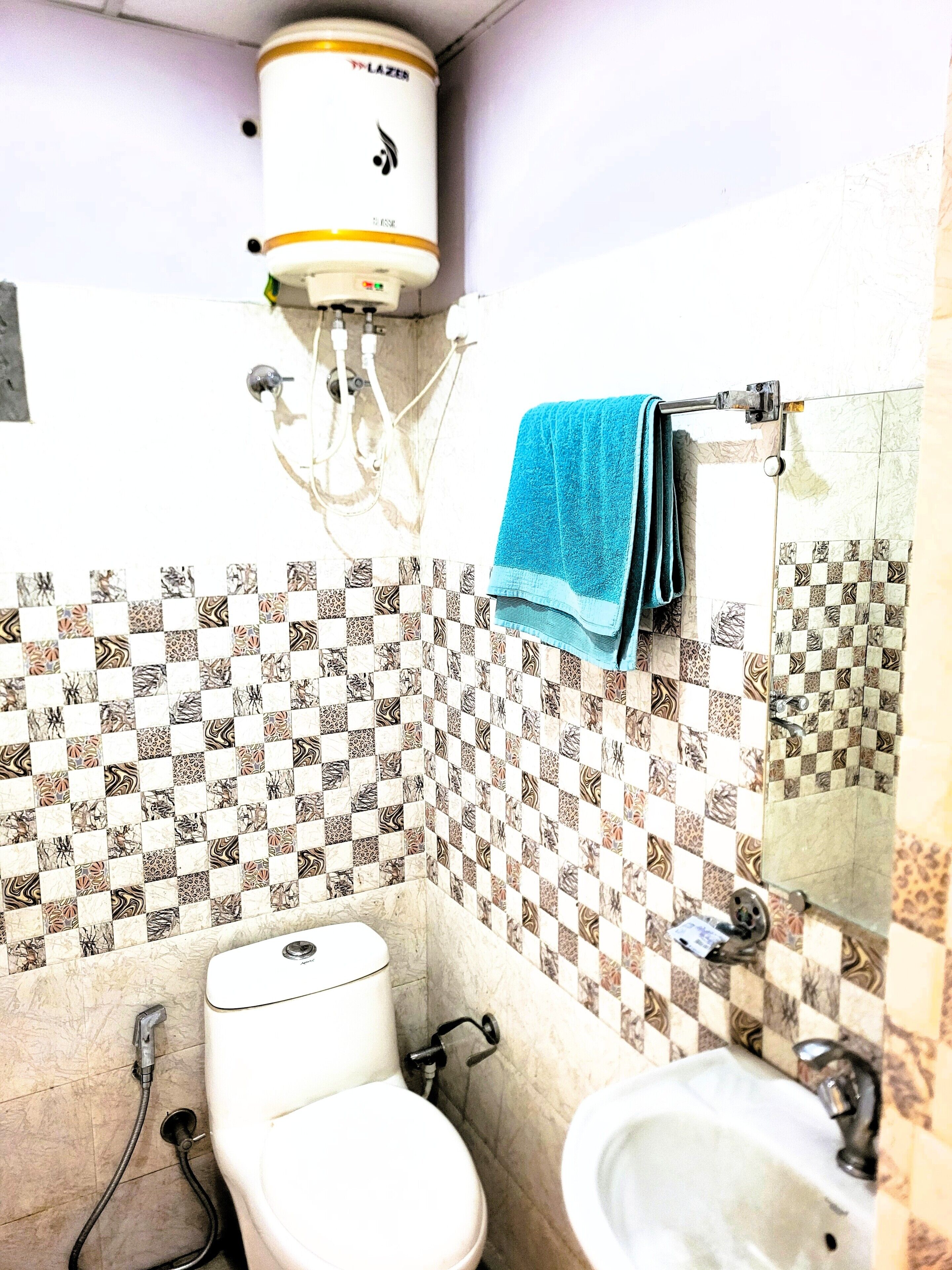 Casa de banho com sanita, bidé e lavatório, com azulejos estampados e um porta-toalhas com uma toalha azul.