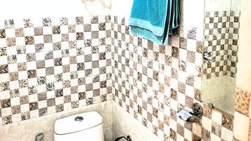Casa de banho com sanita, bidé e lavatório, com azulejos estampados e um porta-toalhas com uma toalha azul.