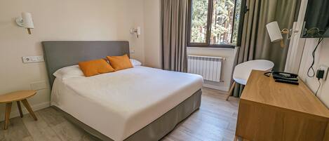 Une chambre d’hôtel avec un lit, un bureau, une chaise, une fenêtre avec des rideaux et un radiateur.