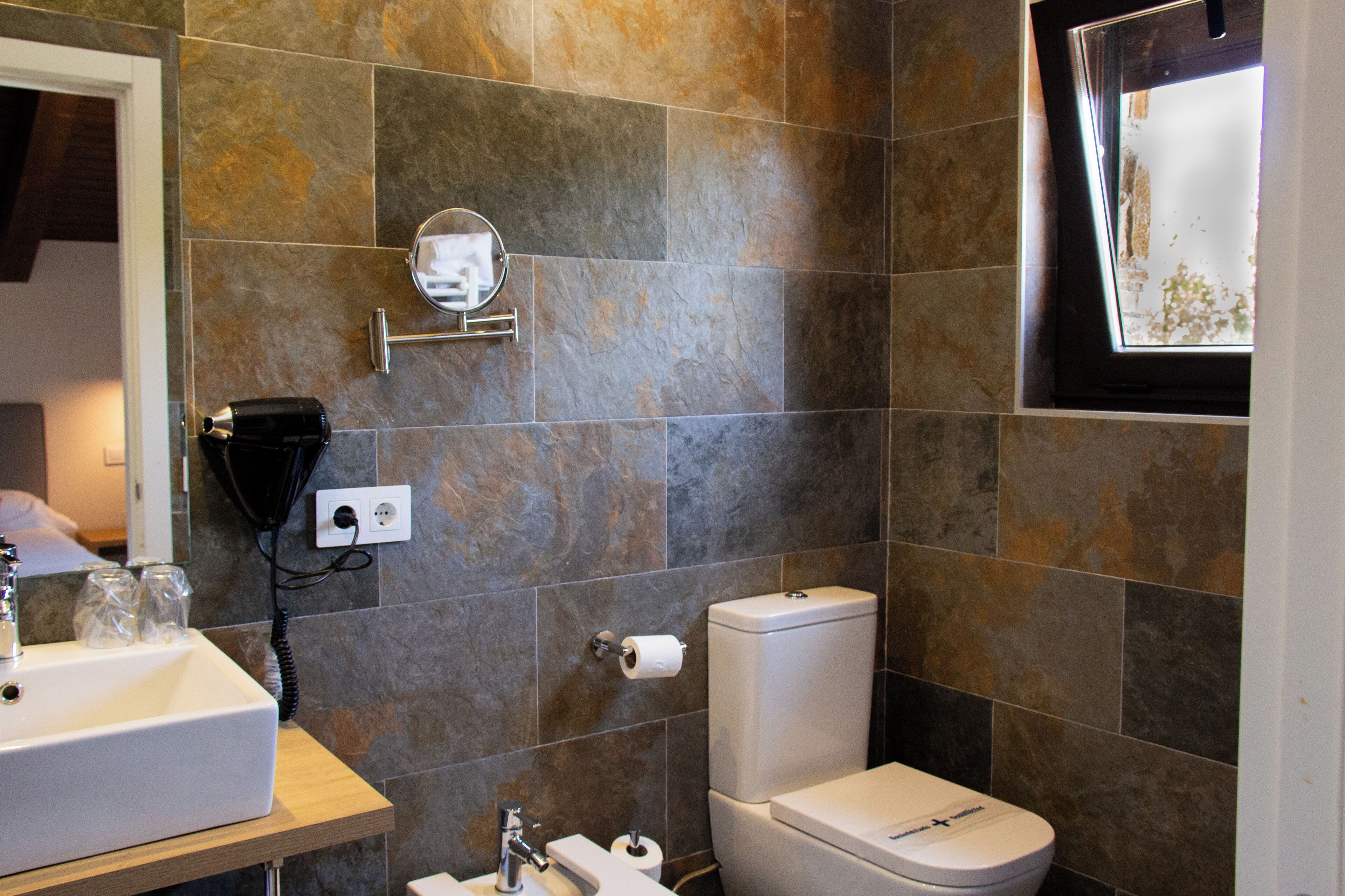 Un baño con lavabo, espejo, inodoro y ventana.