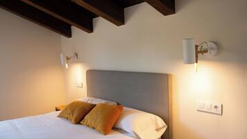 A neatly made bed with two pillows, a wooden nightstand, and a wall-mounted light fixture.