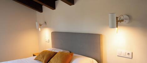 A neatly made bed with two pillows, a wooden nightstand, and a wall-mounted light fixture.