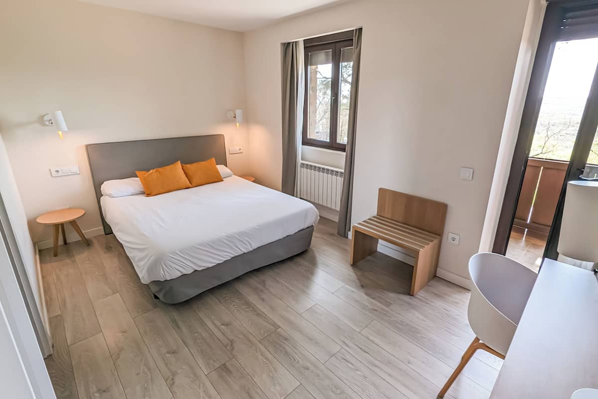 Ein modernes Schlafzimmer mit einem großen Bett, einem kleinen Nachttisch, einer Bank und einem Sessel.
