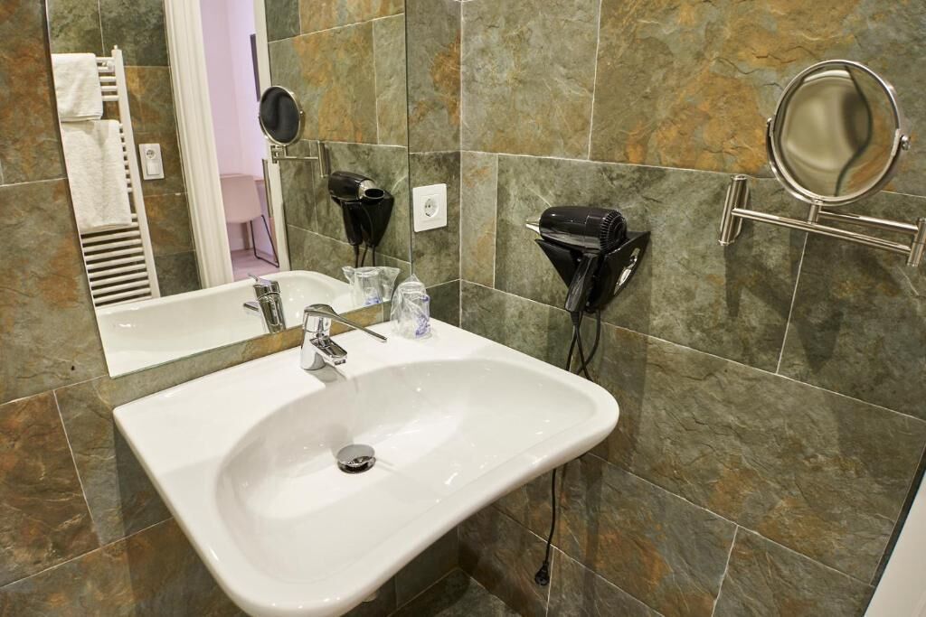 Un baño con un lavamanos blanco, dos secadores de pelo, un espejo y un perchero para toallas.