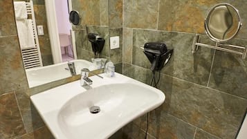 Un baño con un lavamanos blanco, dos secadores de pelo, un espejo y un perchero para toallas.