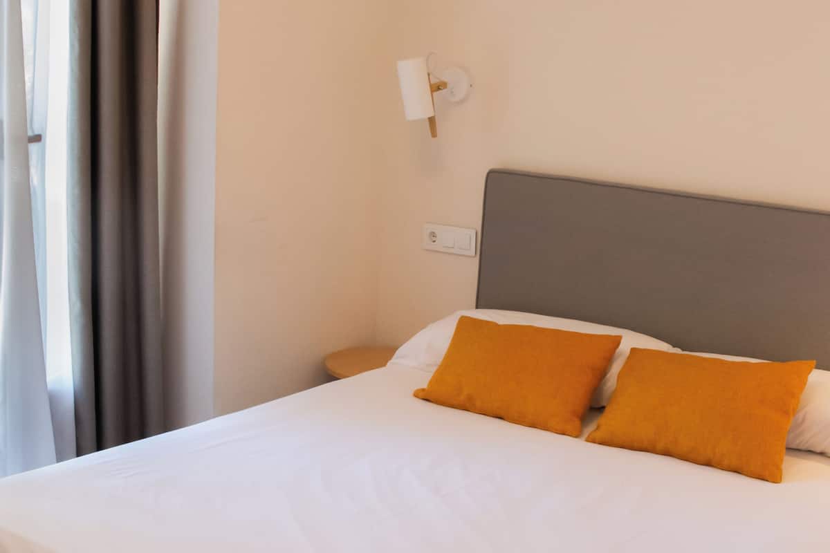 Ein Hotelzimmer mit Bett, Vorhängen, einem Nachttisch und einer Wandlampe.