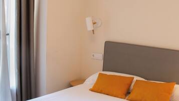 Una habitación de hotel con cama, cortinas, una mesita de noche y una lámpara fijada a la pared.