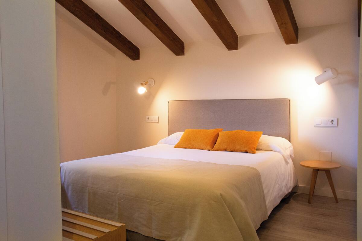 Ein Schlafzimmer mit Bett, Holzbalken, einem Nachttisch und einer Wandleuchte.