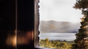 A view through a window with a torn edge, revealing a landscape with mountains, a body of water, and trees. - Hotel Villalucerna (Vigo)